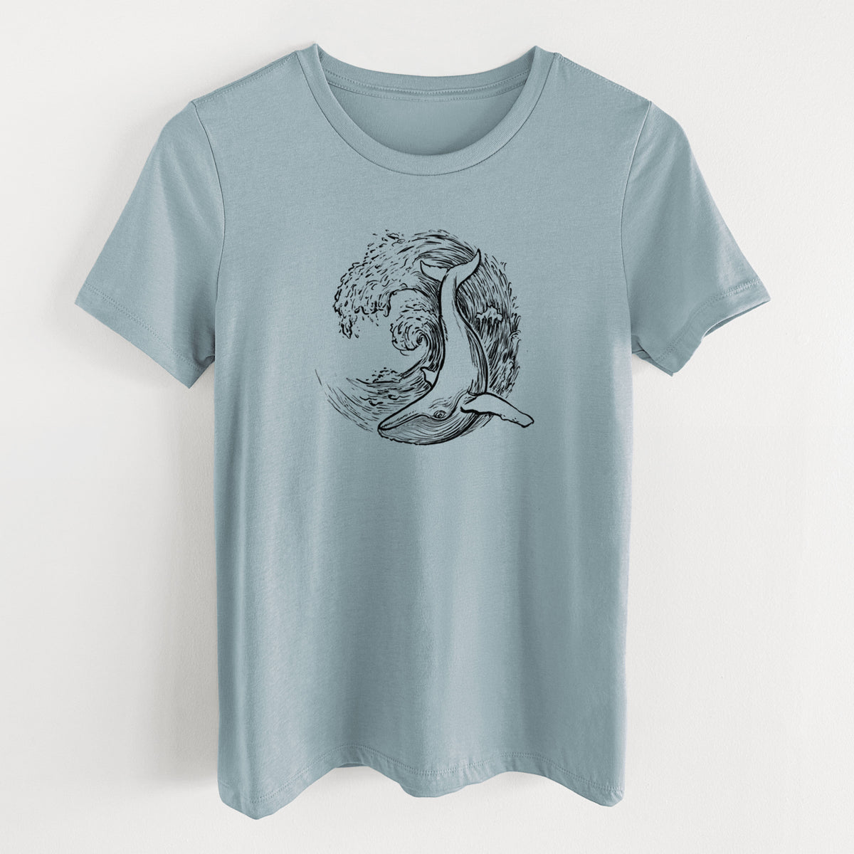 Vintage denim women's relaxed fit cotton t-shirt laid flat, printed with a black ink illustration of a humpback whale swimming inside a curling ocean wave.