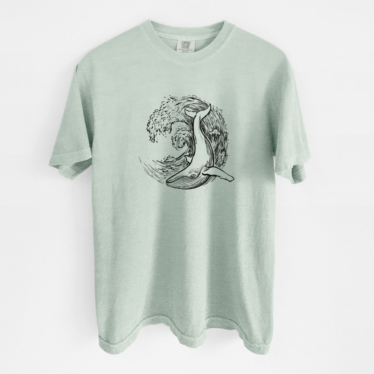 Bay green Comfort Colors t-shirt laid flat, printed with a black ink illustration of a humpback whale swimming inside a curling ocean wave.