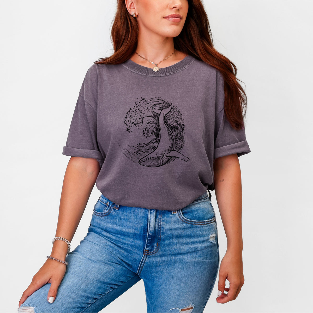 Woman wearing a Comfort Colors t-shirt printed with a black ink illustration of a humpback whale swimming inside a curling ocean wave.