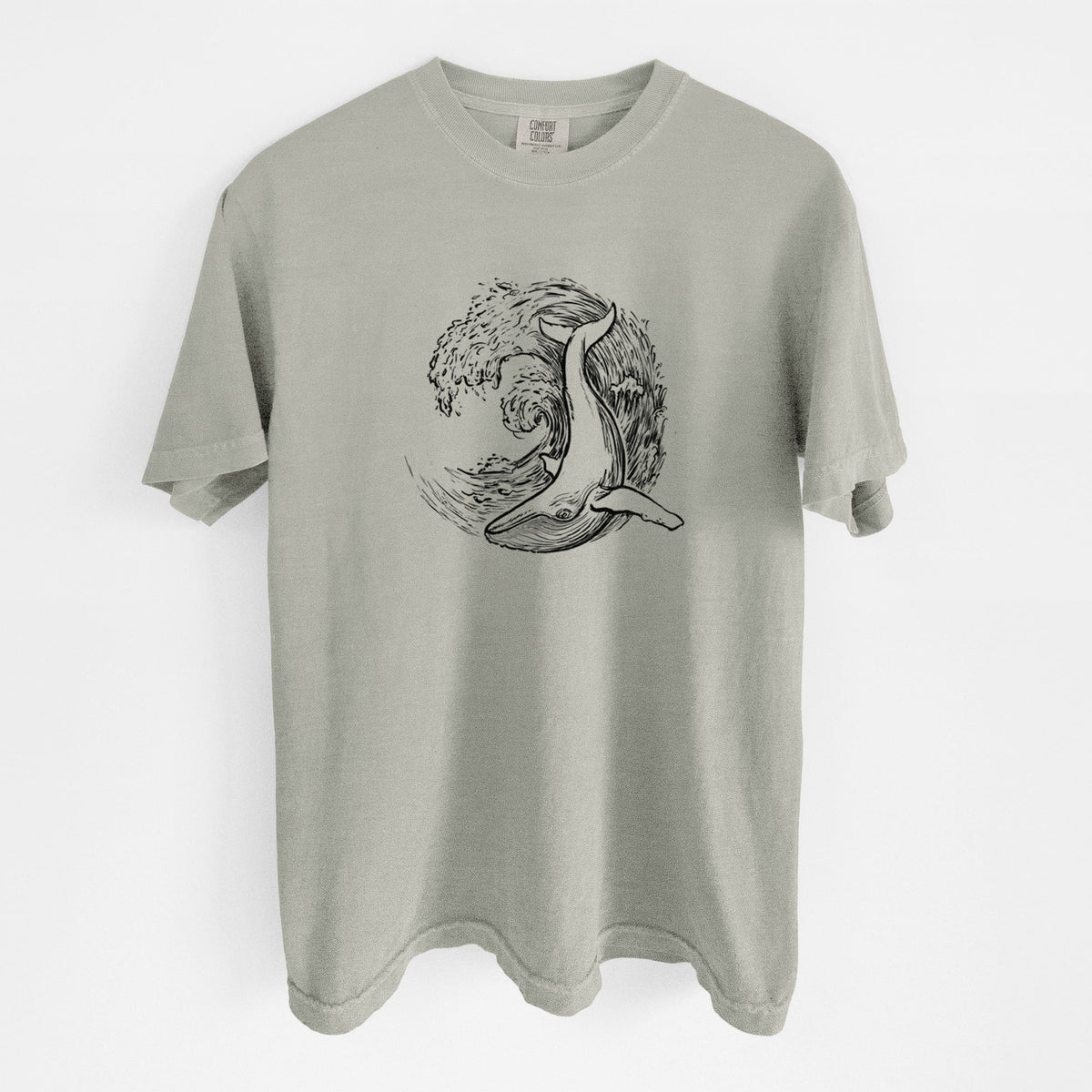 Sandstone beige Comfort Colors t-shirt laid flat, printed with a black ink illustration of a humpback whale swimming inside a curling ocean wave.