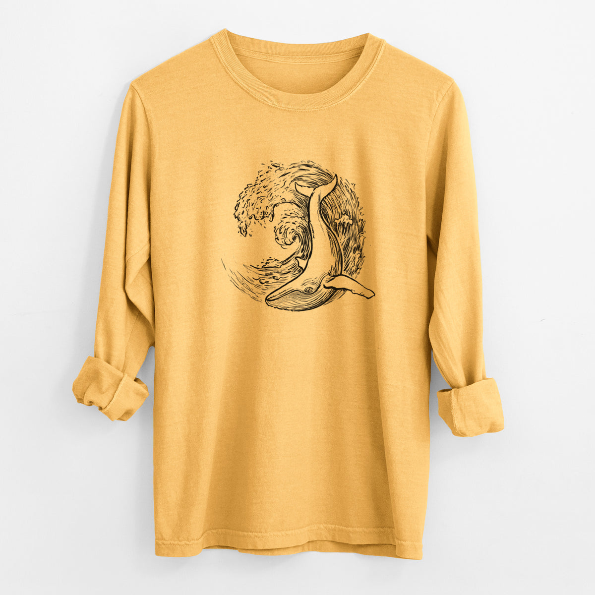 Golden wheat yellow Comfort Colors long sleeve shirt laid flat with the cuffs rolled, printed with a black ink illustration of a humpback whale swimming inside a curling ocean wave.