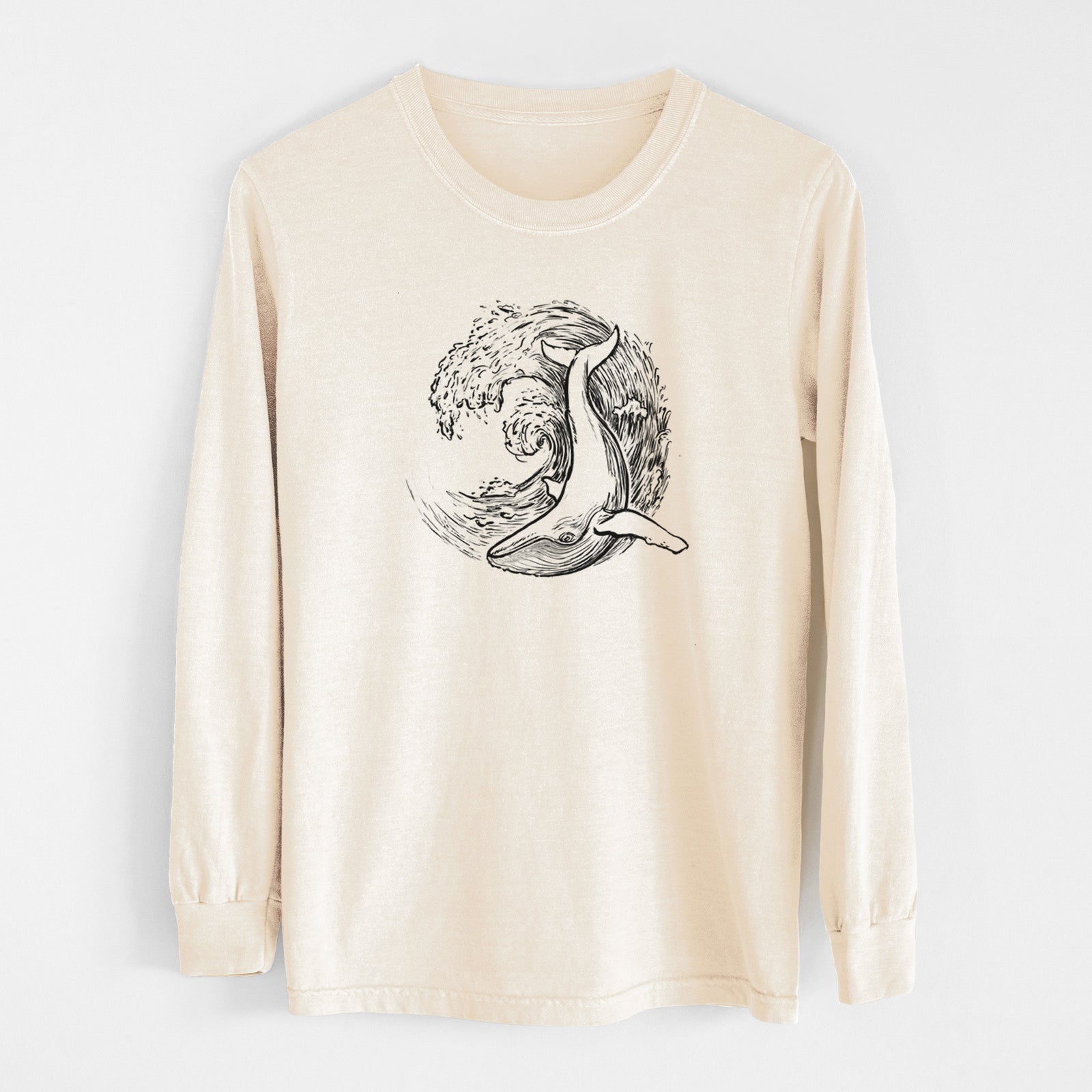 Ivory Comfort Colors long sleeve shirt laid flat, printed with a black ink illustration of a humpback whale swimming inside a curling ocean wave.