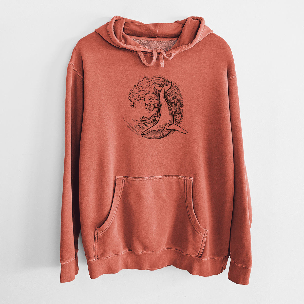 Amber orange pigment dyed hoodie laid flat, printed with a black ink illustration of a humpback whale swimming inside a curling ocean wave.