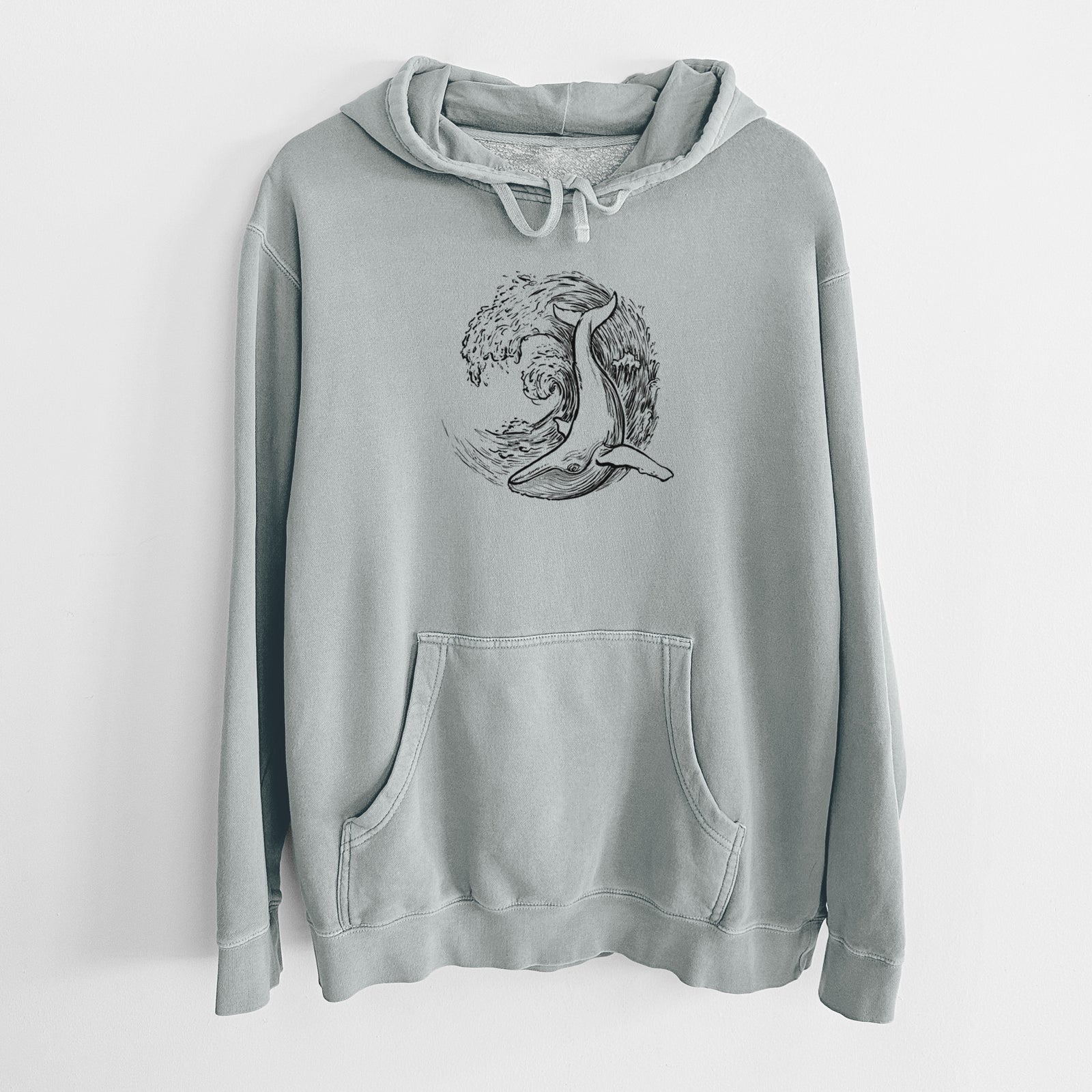 Sage green pigment dyed hoodie laid flat, printed with a black ink illustration of a humpback whale swimming inside a curling ocean wave.