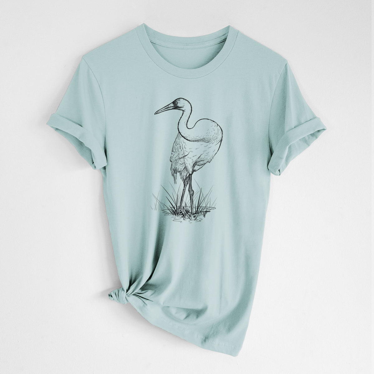 Dusty blue lightweight cotton t-shirt laid flat with the sleeves rolled, printed with a detailed black ink illustration of a whooping crane standing in grass.
