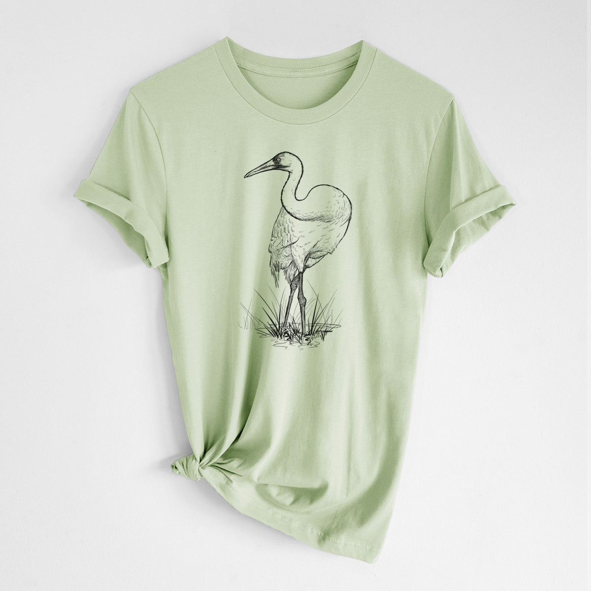 Spring green lightweight cotton t-shirt laid flat with the sleeves rolled, printed with a detailed black ink illustration of a whooping crane standing in grass.