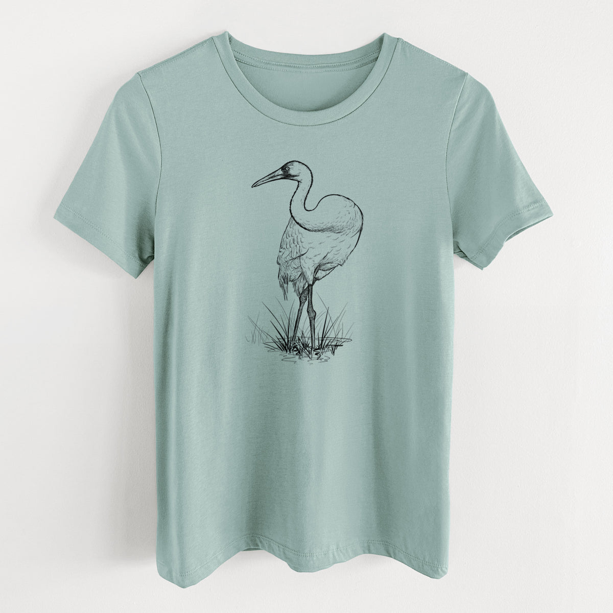 Dusty blue women's relaxed fit cotton t-shirt laid flat, printed with a detailed black ink illustration of a whooping crane standing in grass.