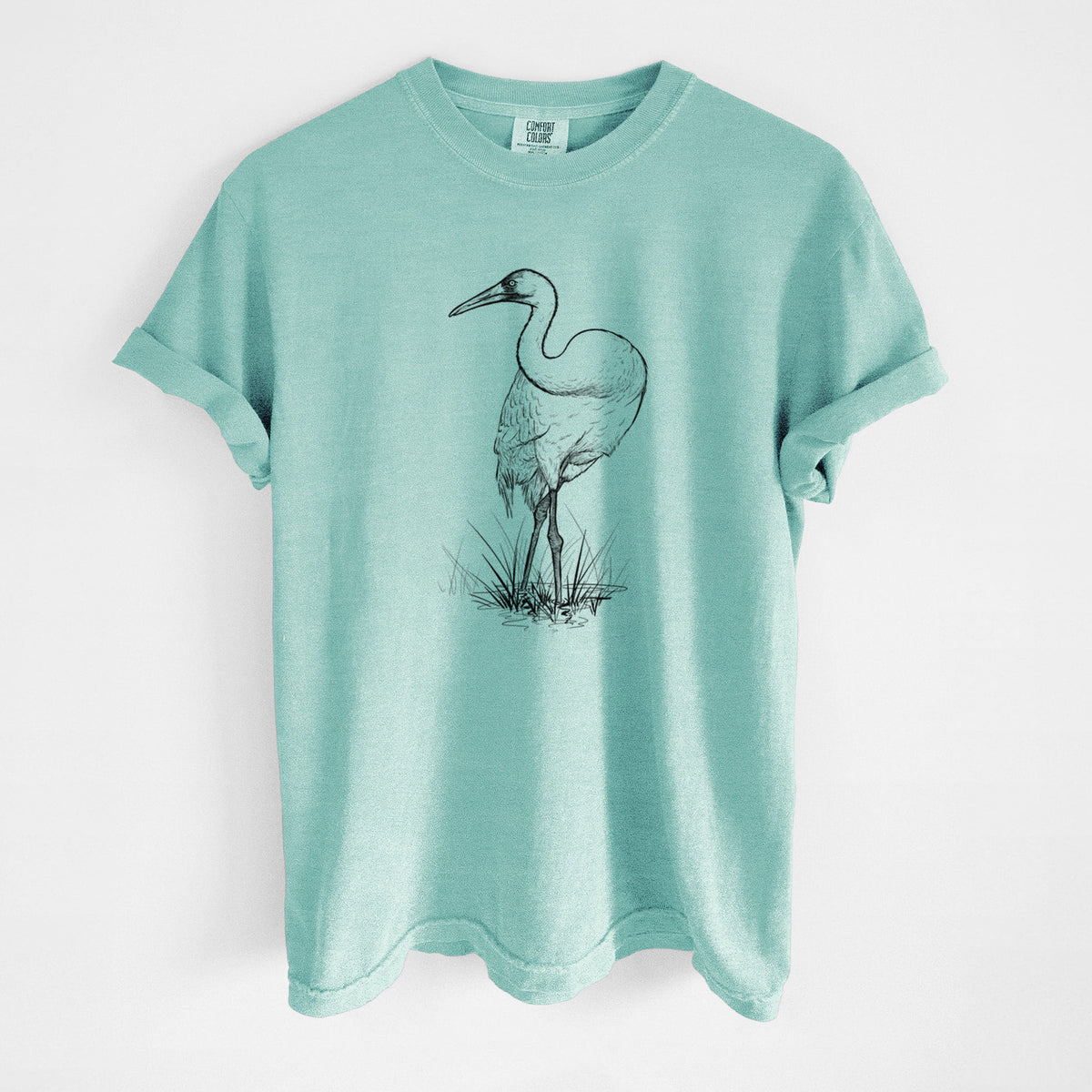 Chalky mint Comfort Colors t-shirt laid flat, printed with a detailed black ink illustration of a whooping crane standing in grass.