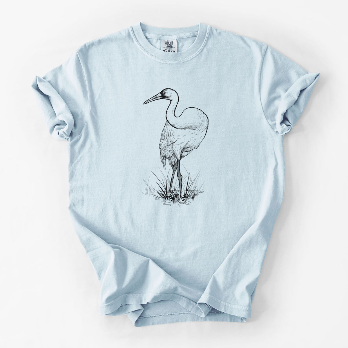 Chambray blue Comfort Colors t-shirt laid flat, printed with a detailed black ink illustration of a whooping crane standing in grass.