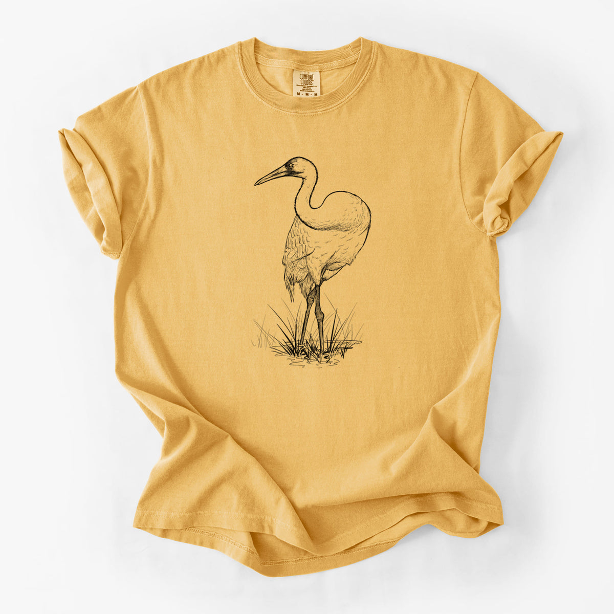 Golden wheat yellow Comfort Colors t-shirt laid flat, printed with a detailed black ink illustration of a whooping crane standing in grass.