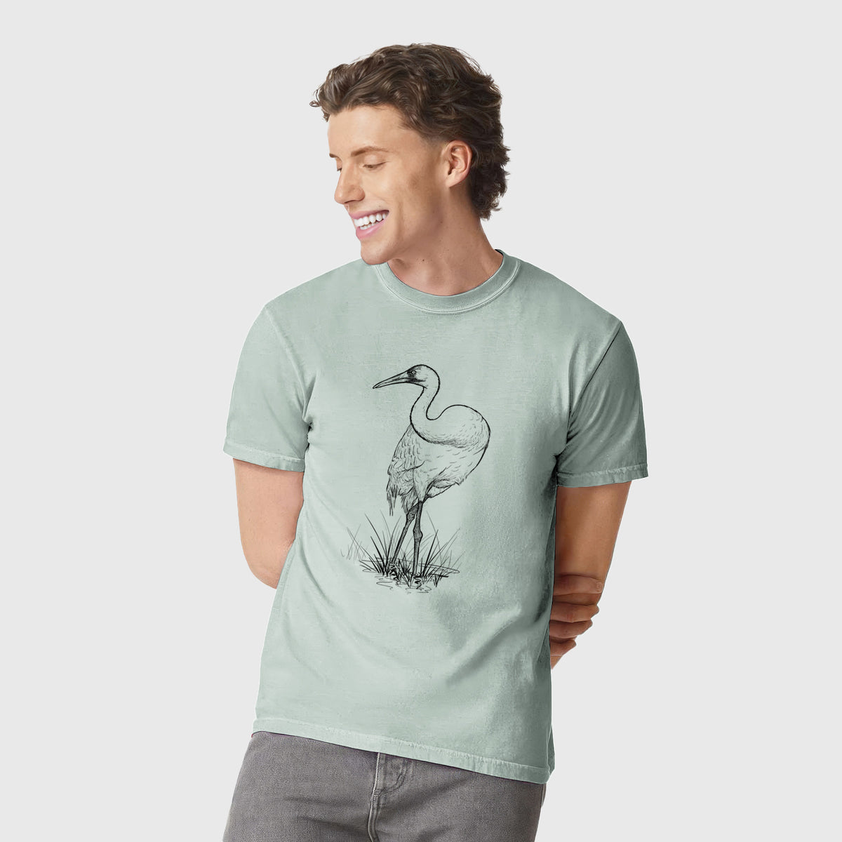 Man wearing a Comfort Colors t-shirt printed with a detailed black ink illustration of a whooping crane standing in grass.