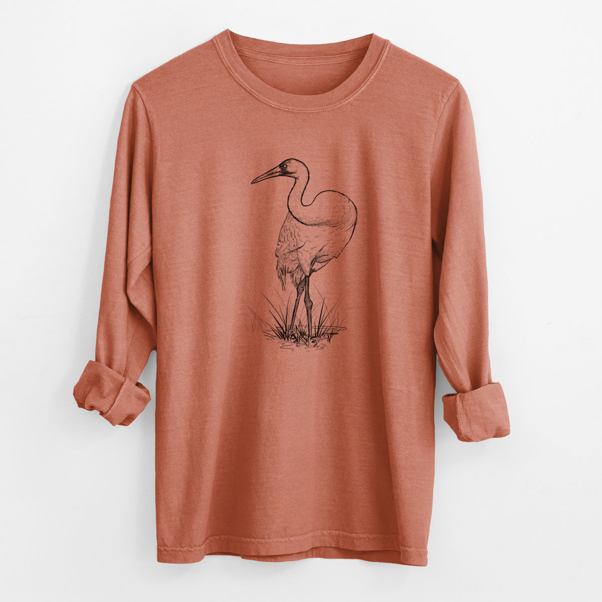 Yam burnt orange Comfort Colors long sleeve shirt laid flat with the cuffs rolled, printed with a detailed black ink illustration of a whooping crane standing in grass.