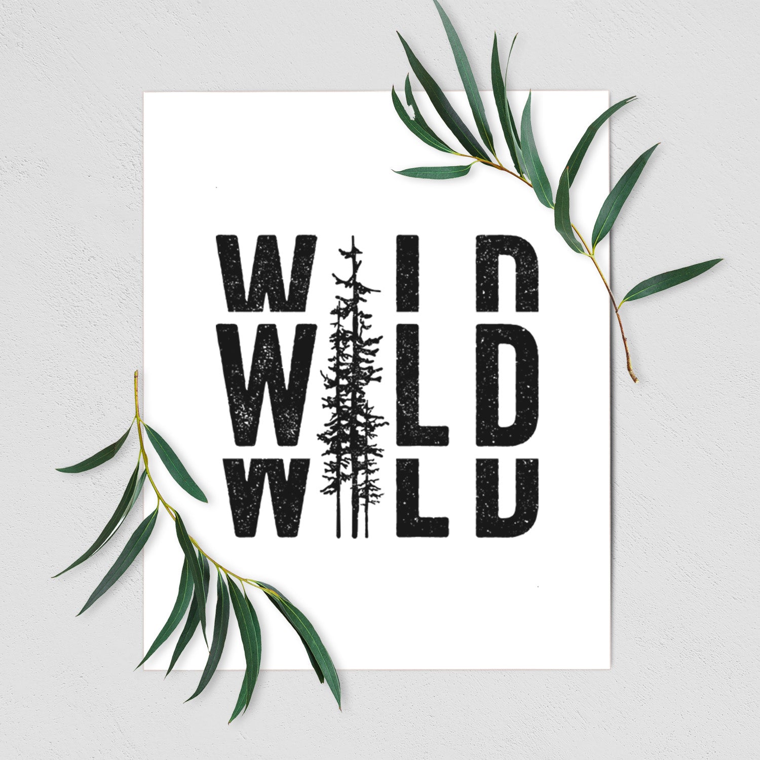 Art print of bold black text reading WILD stacked three times, with a tall pine tree forming the letter I, shown with eucalyptus leaves.