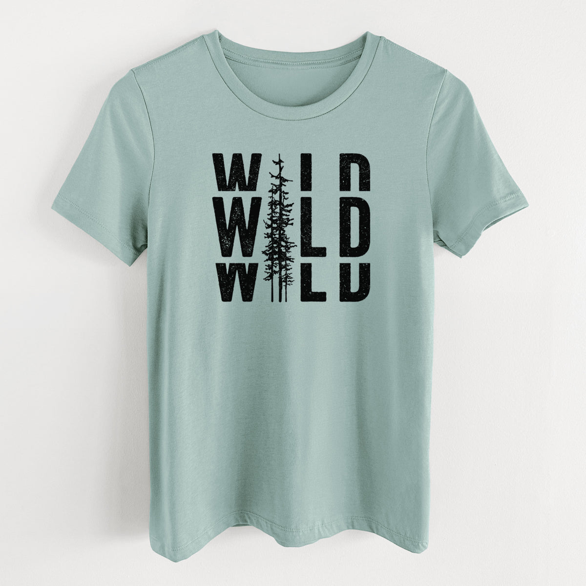 Dusty blue women's relaxed fit cotton t-shirt laid flat, printed with bold black text reading WILD stacked three times, with a tall pine tree forming the letter I.