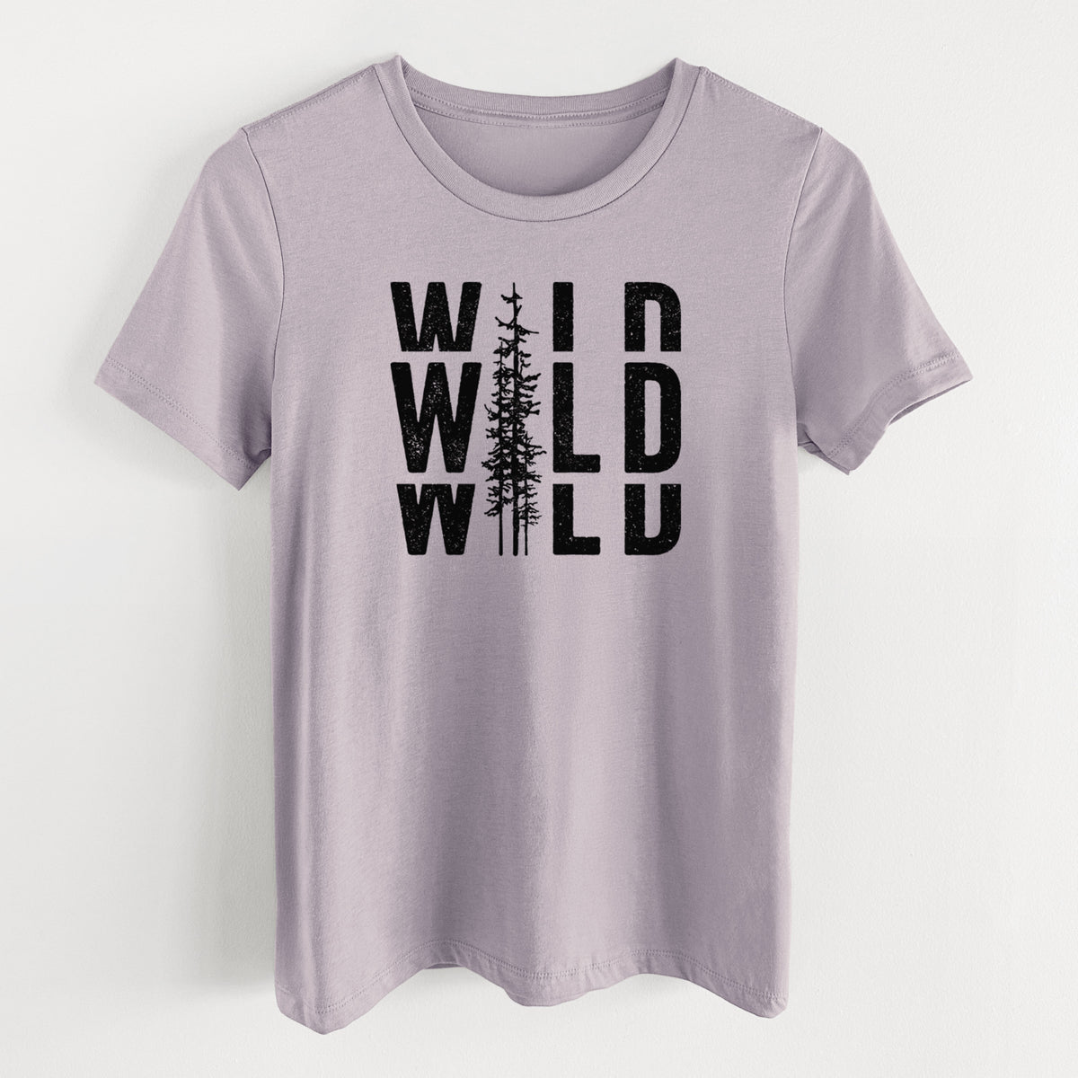 Light violet women's relaxed fit cotton t-shirt laid flat, printed with bold black text reading WILD stacked three times, with a tall pine tree forming the letter I.