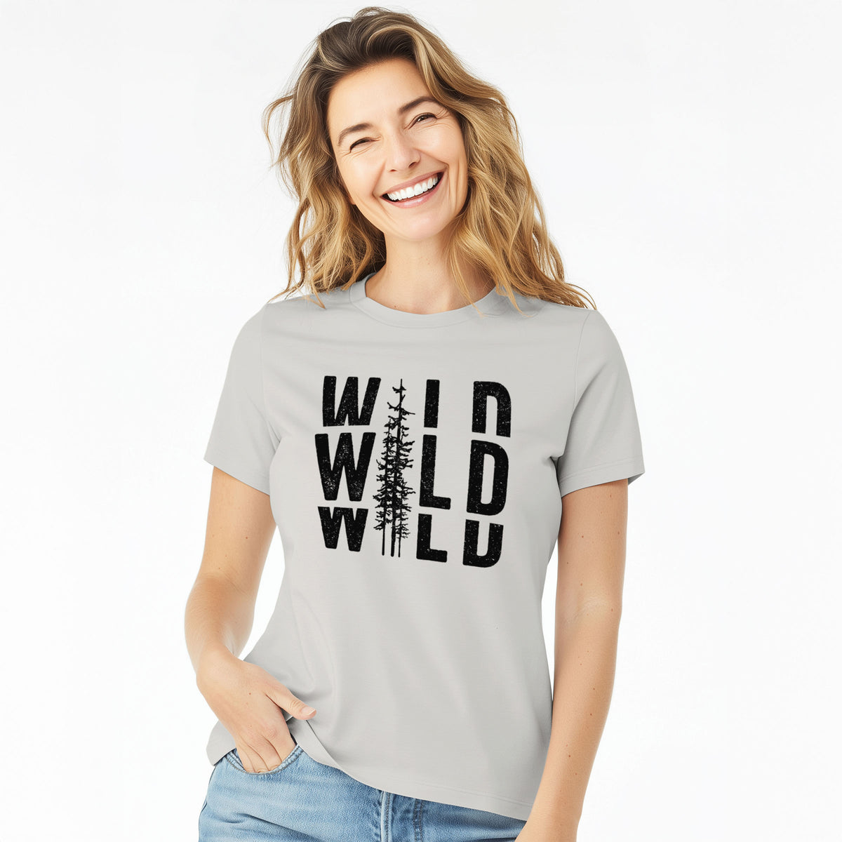 Woman wearing a lunar grey women's relaxed fit cotton t-shirt printed with bold black text reading WILD stacked three times, with a tall pine tree forming the letter I.