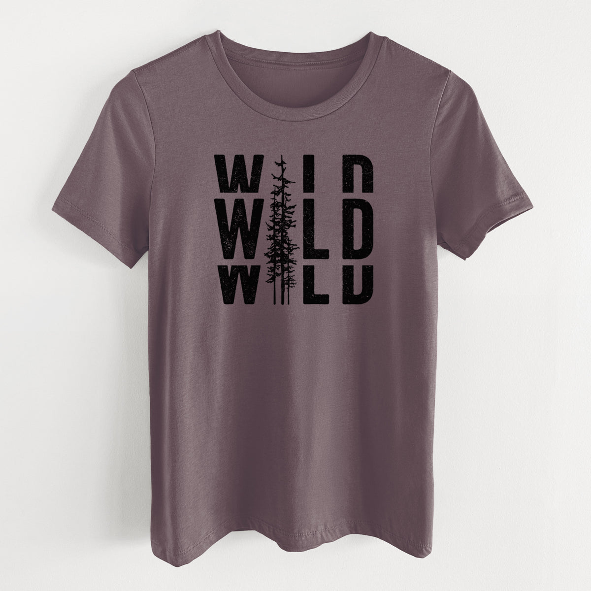 Purple storm women's relaxed fit cotton t-shirt laid flat, printed with bold black text reading WILD stacked three times, with a tall pine tree forming the letter I.