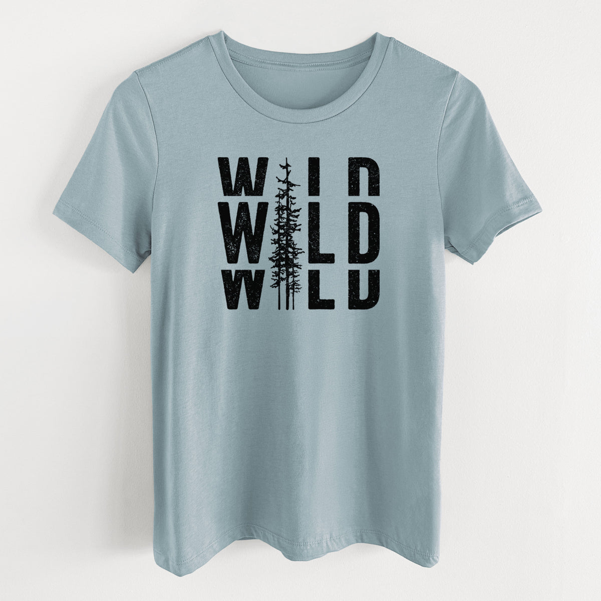 Vintage denim women's relaxed fit cotton t-shirt laid flat, printed with bold black text reading WILD stacked three times, with a tall pine tree forming the letter I.