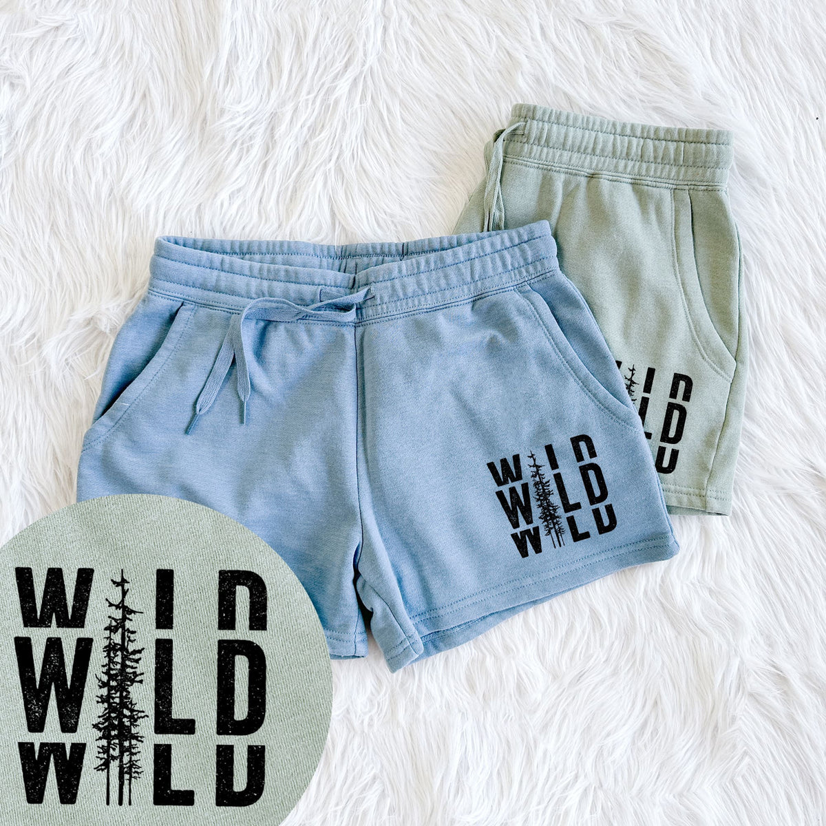 Two pairs of Cali Wave shorts in different colors printed with bold black text reading WILD stacked three times, with a tall pine tree forming the letter I, with a close-up of the print.