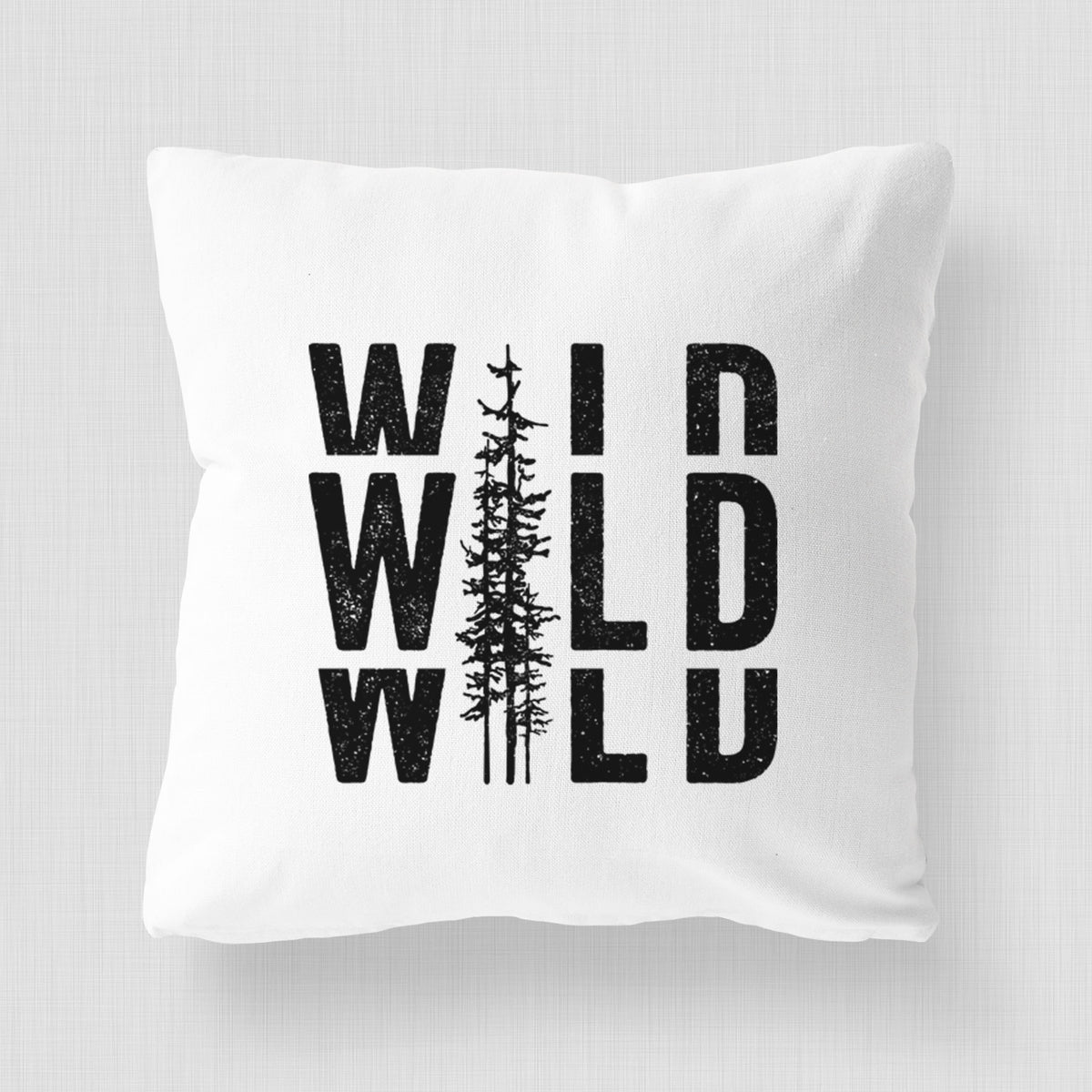 White pillow cover printed with bold black text reading WILD stacked three times, with a tall pine tree forming the letter I.