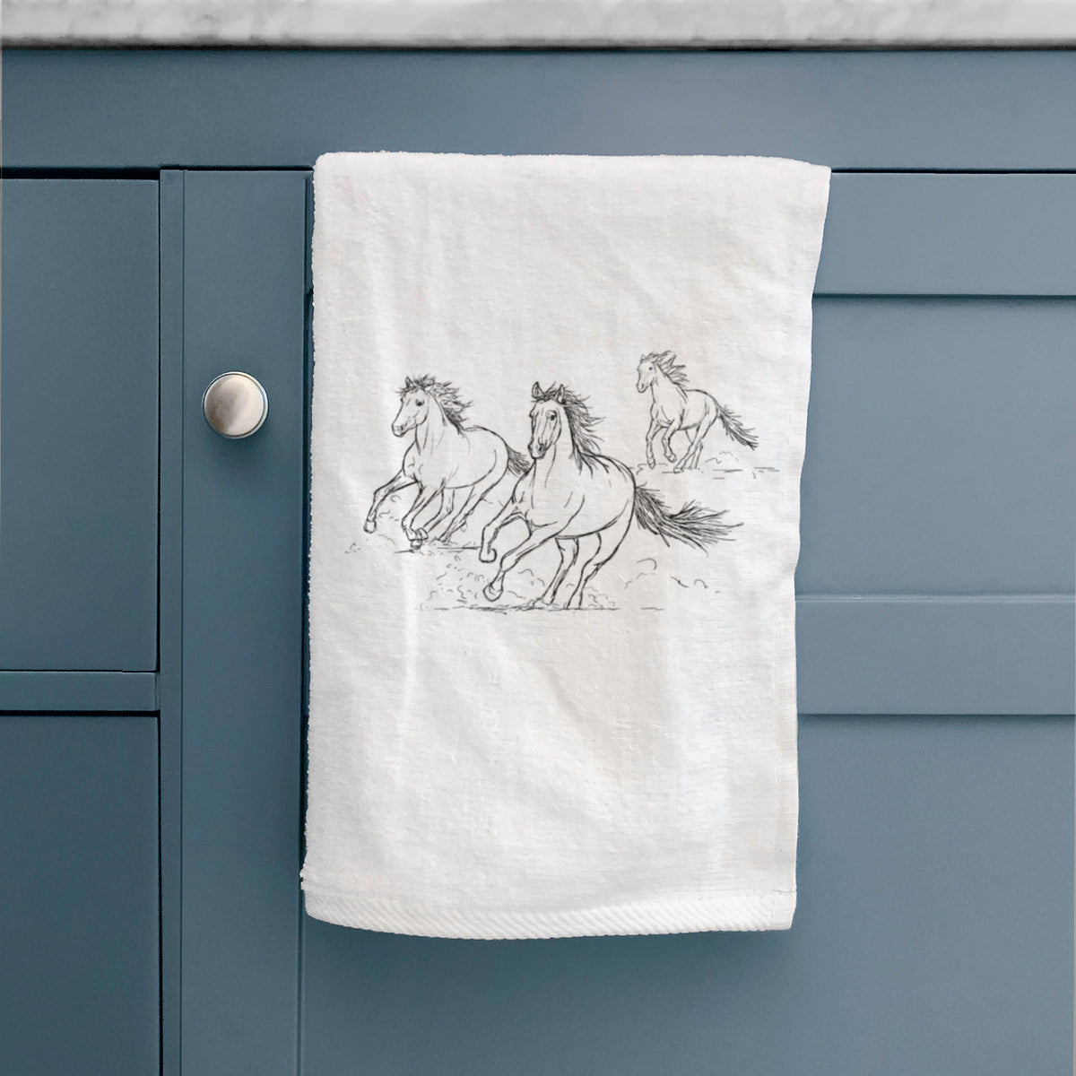 White hand towel printed with a black ink illustration of three wild horses galloping, hanging on a cabinet door.