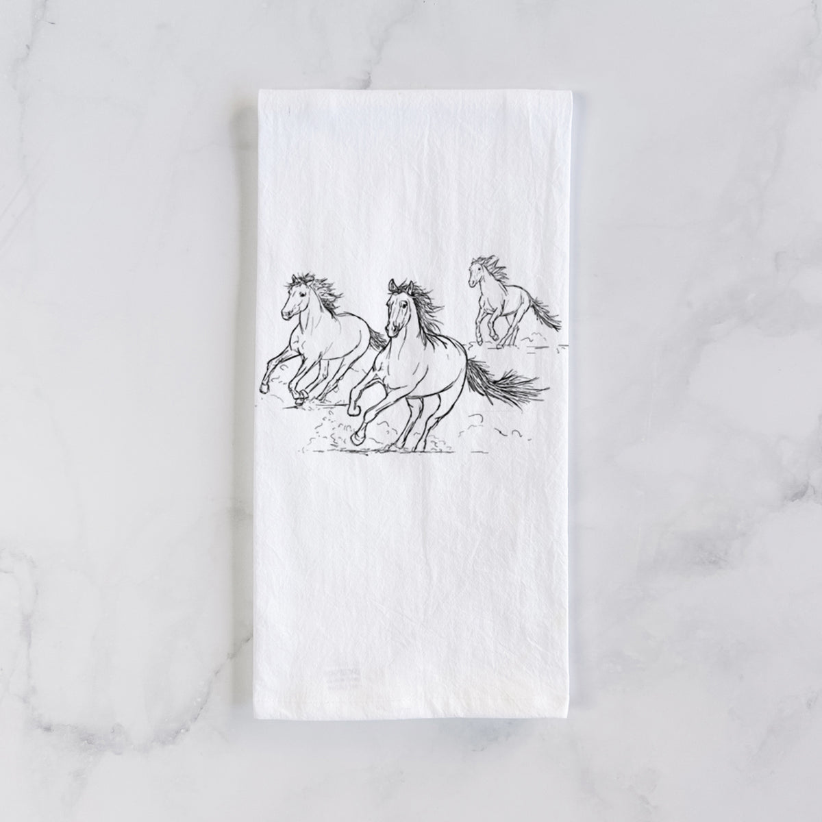 White cotton tea towel laid flat on marble, printed with a black ink illustration of three wild horses galloping.