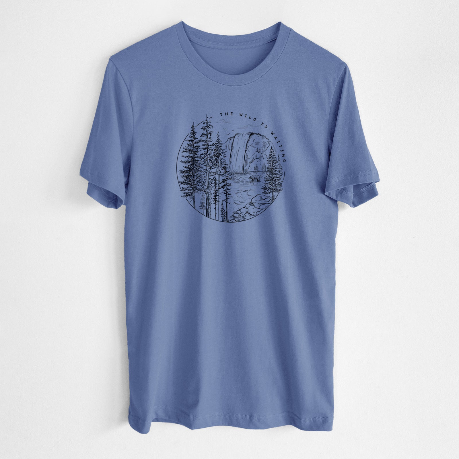 Blue bell lightweight cotton t-shirt laid flat, printed with a round black ink scene of a waterfall, pine trees and a river, with the words The Wild Is Waiting.