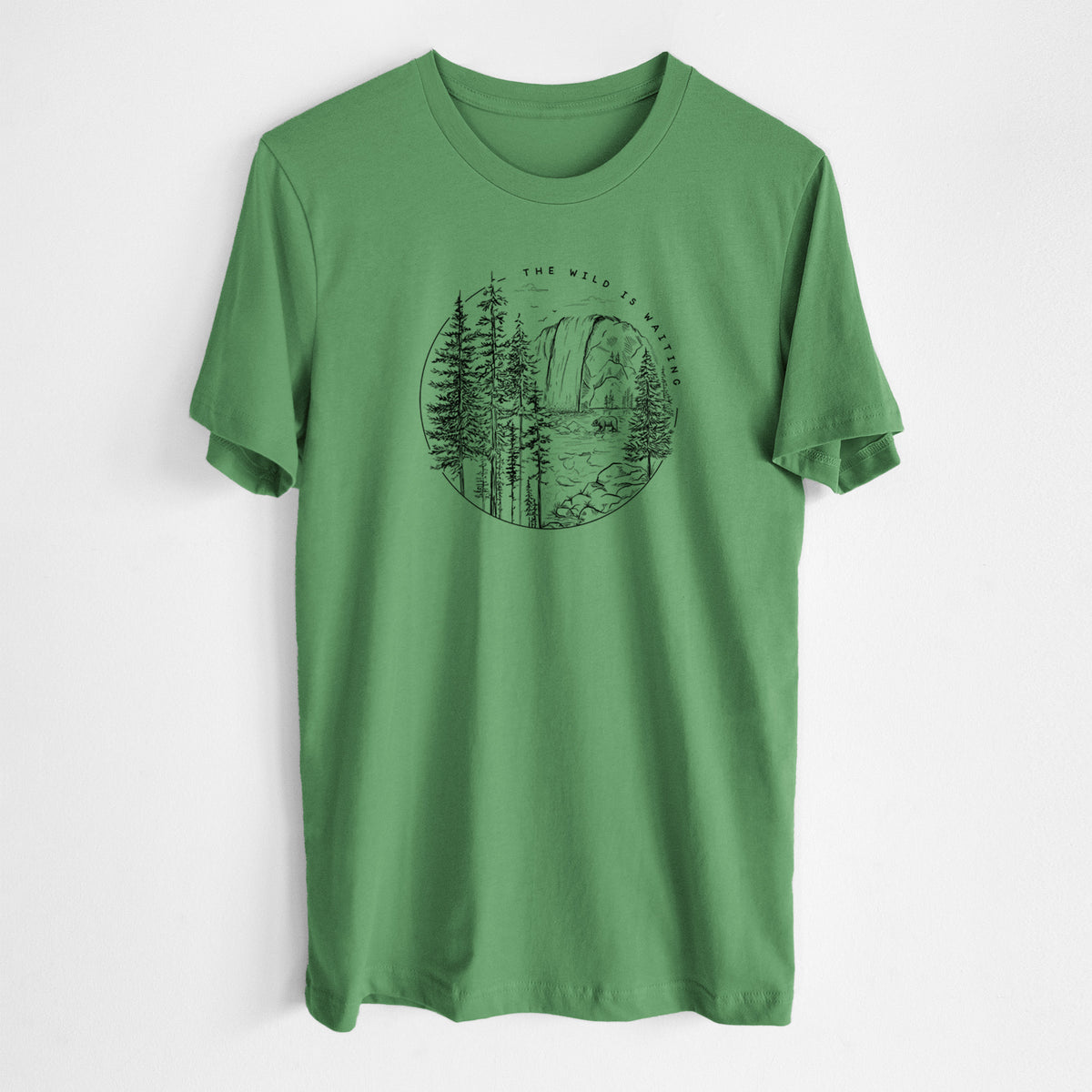 Leaf green lightweight cotton t-shirt laid flat, printed with a round black ink scene of a waterfall, pine trees and a river, with the words The Wild Is Waiting.