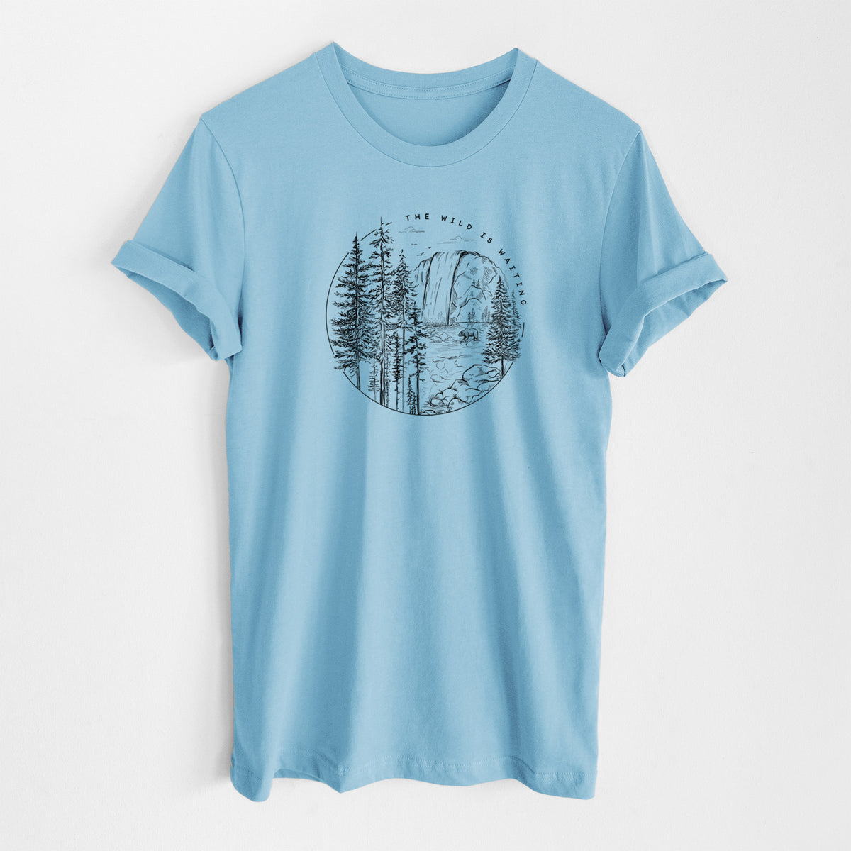 Ocean blue lightweight cotton t-shirt laid flat, printed with a round black ink scene of a waterfall, pine trees and a river, with the words The Wild Is Waiting.