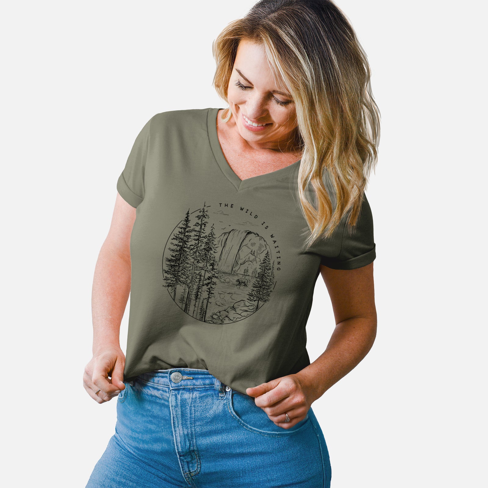 Turquoise women's relaxed fit cotton V-neck t-shirt laid flat, printed with a round black ink scene of a waterfall, pine trees and a river, with the words The Wild Is Waiting.