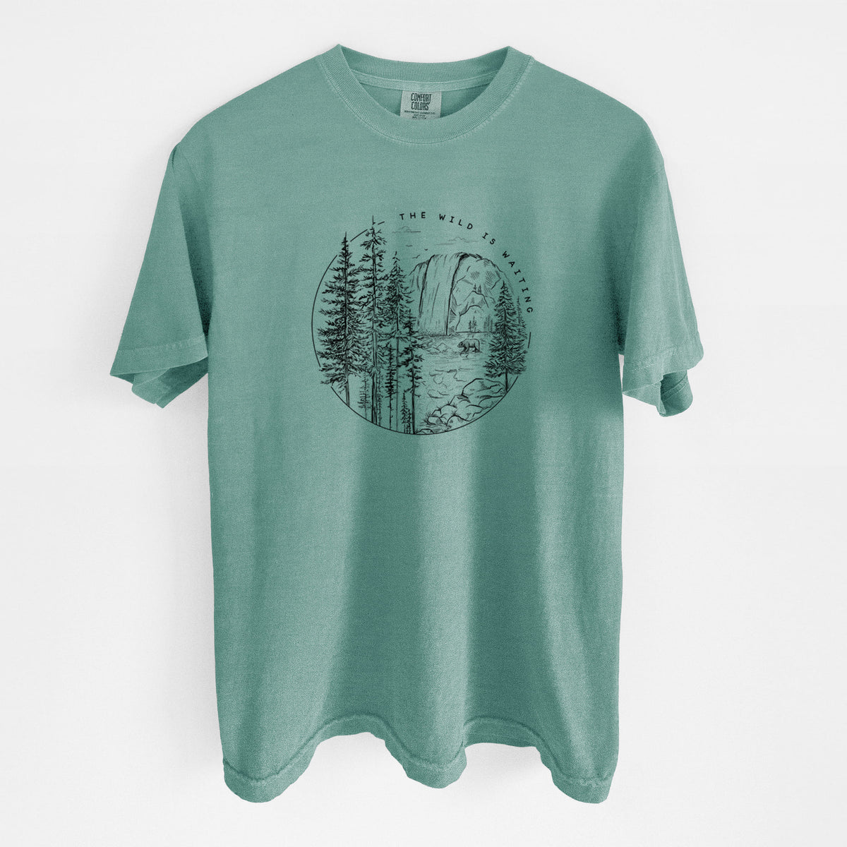 Reef green Comfort Colors t-shirt laid flat, printed with a round black ink scene of a waterfall, pine trees and a river, with the words The Wild Is Waiting.