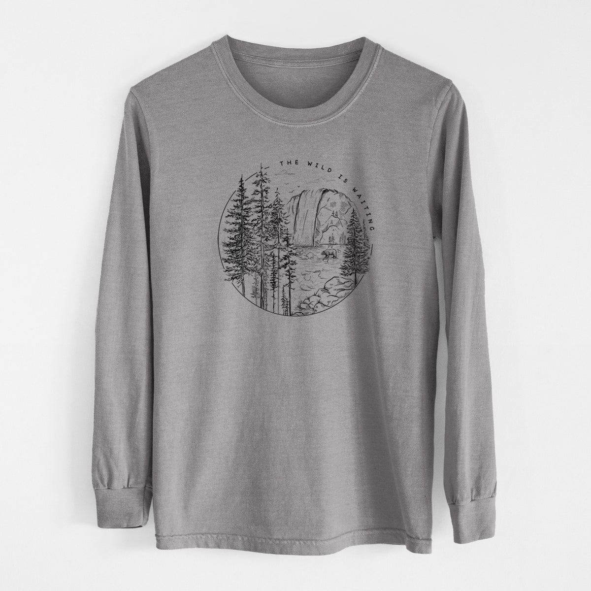 Grey Comfort Colors long sleeve shirt laid flat, printed with a round black ink scene of a waterfall, pine trees and a river, with the words The Wild Is Waiting.