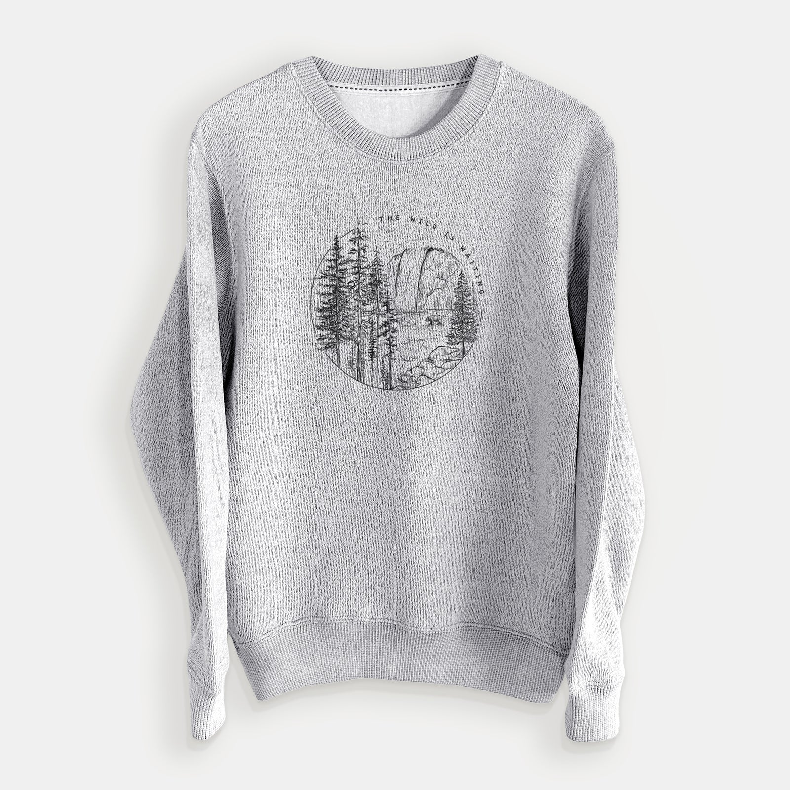 Salt and pepper knit sweatshirt laid flat, printed with a round black ink scene of a waterfall, pine trees and a river, with the words The Wild Is Waiting.