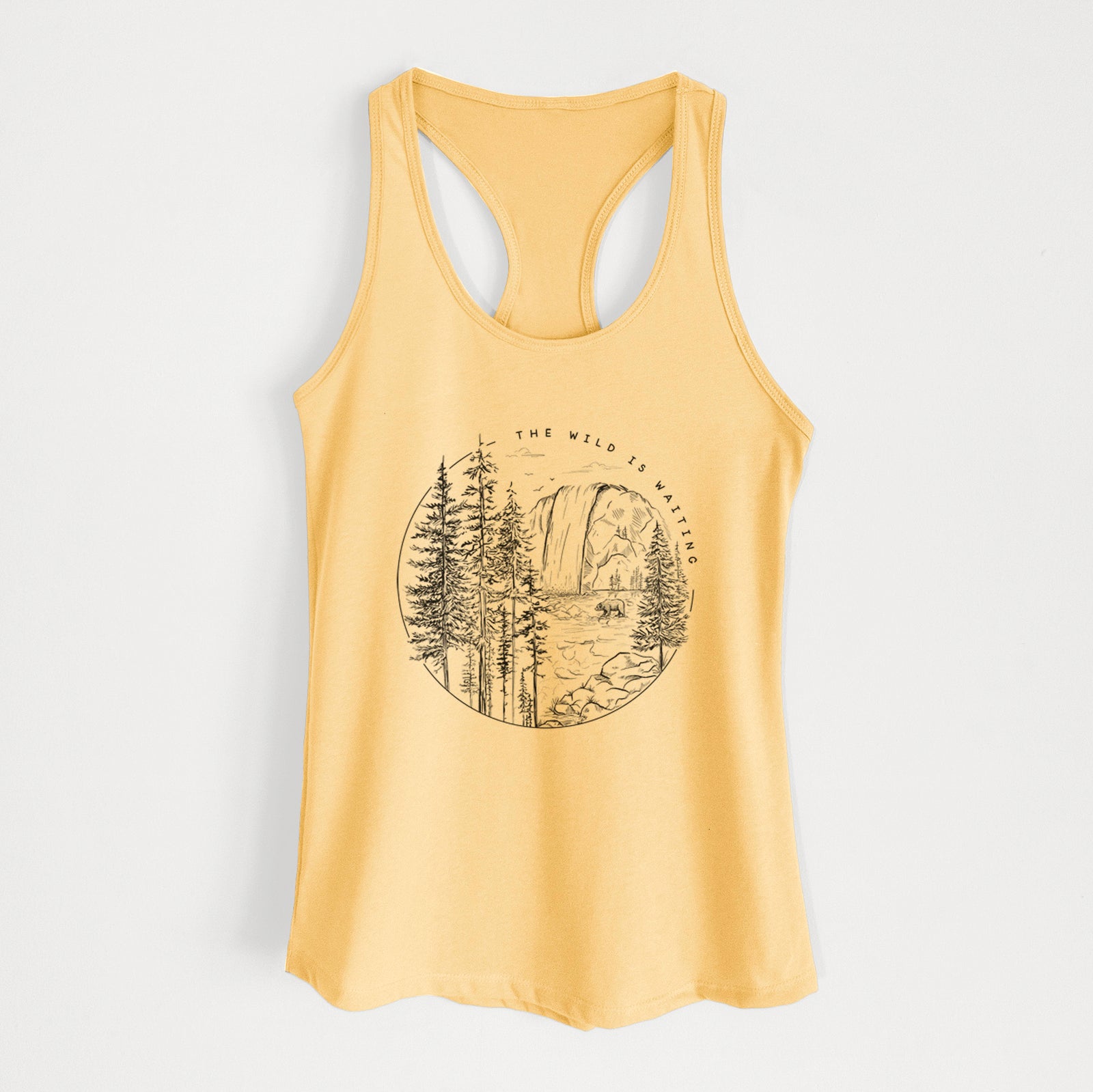 Banana cream women's racerback tank top laid flat, printed with a round black ink scene of a waterfall, pine trees and a river, with the words The Wild Is Waiting.