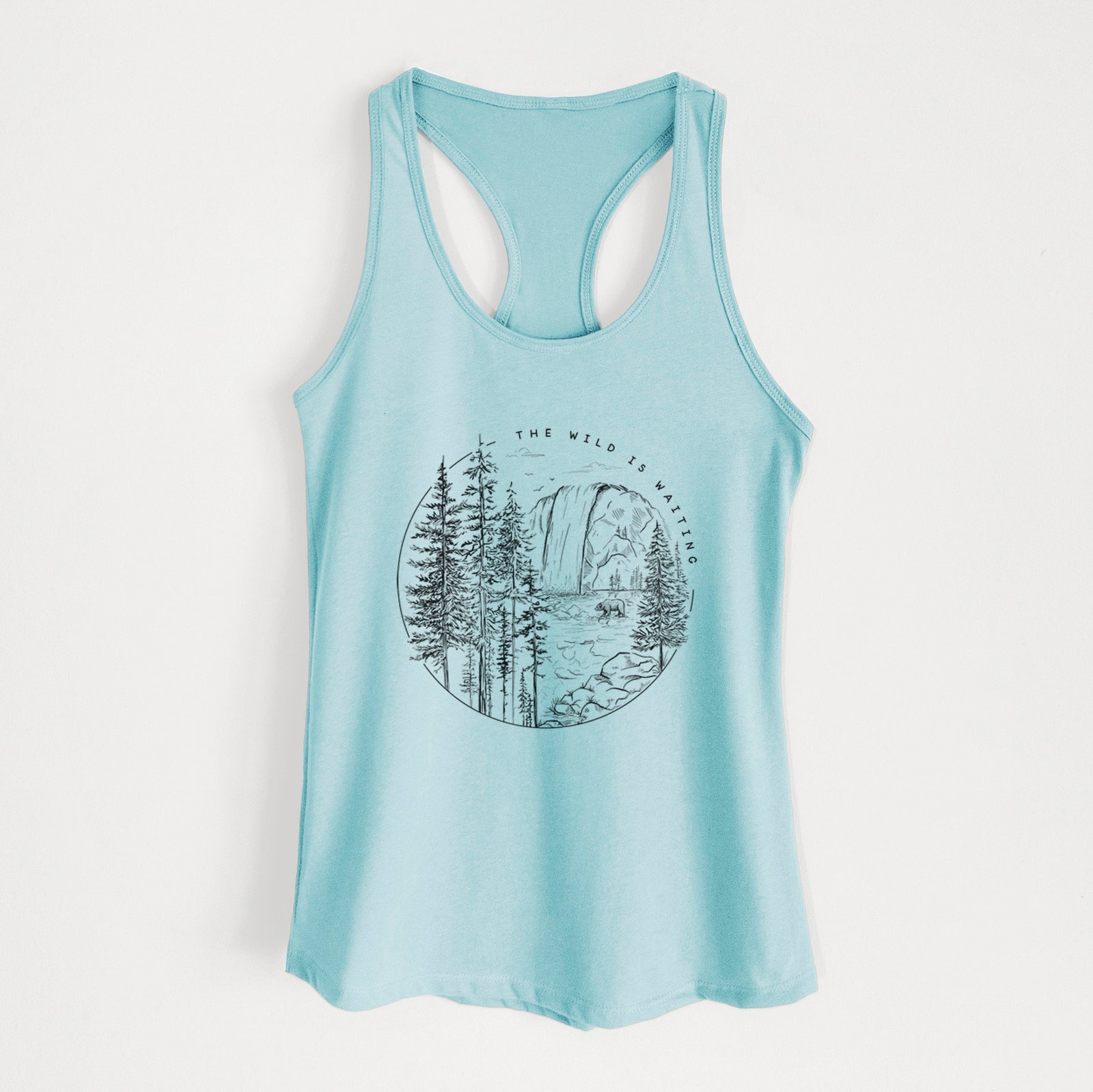Banana cream women's racerback tank top laid flat, printed with a round black ink scene of a waterfall, pine trees and a river, with the words The Wild Is Waiting.