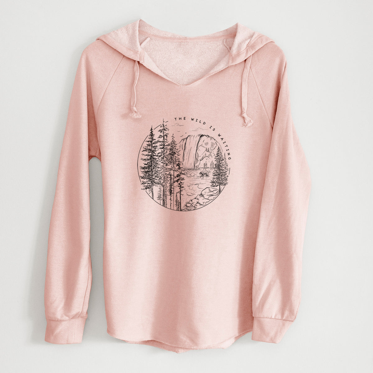 Blush pink women's Cali Wave hooded sweatshirt laid flat, printed with a round black ink scene of a waterfall, pine trees and a river, with the words The Wild Is Waiting.