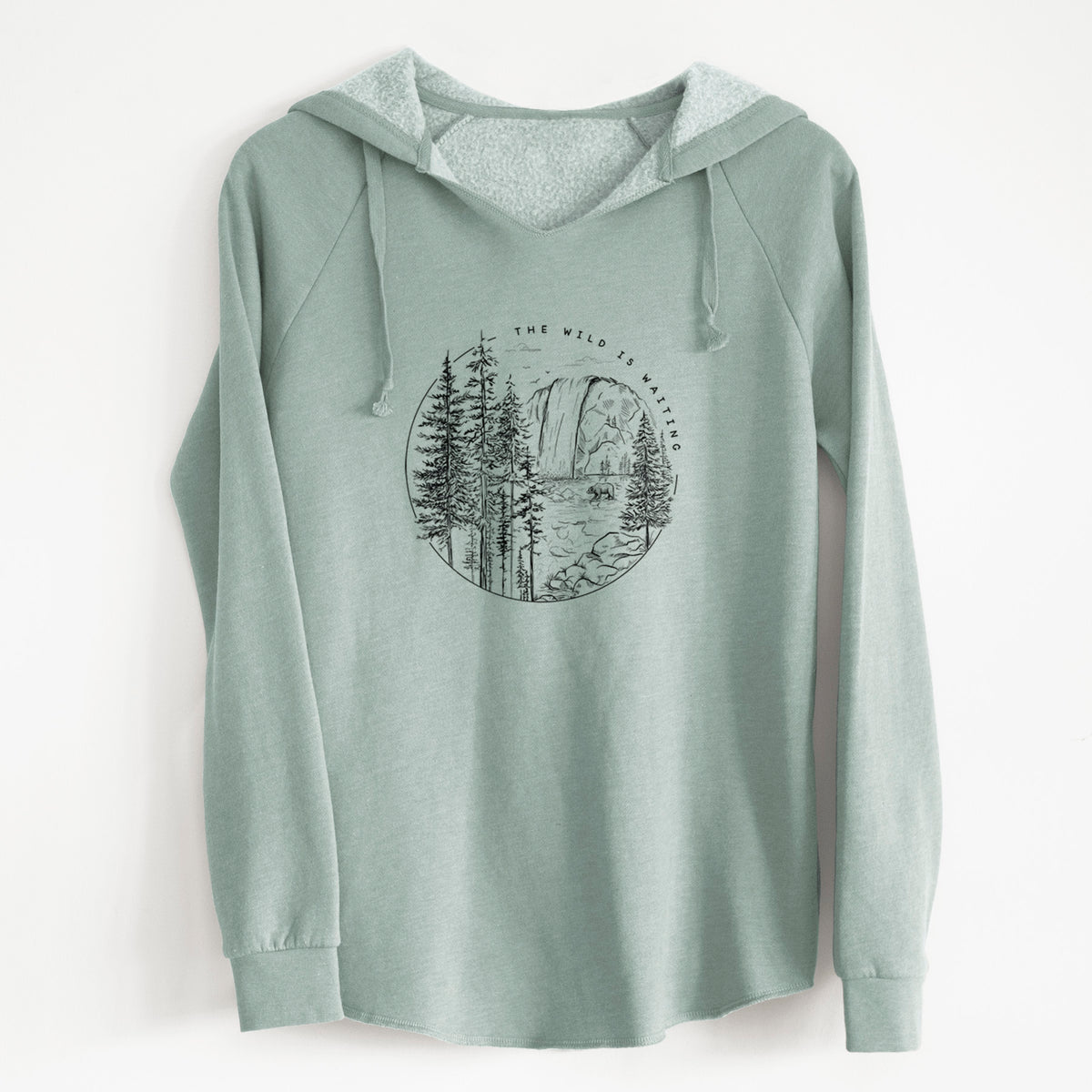 Sage green women's Cali Wave hooded sweatshirt laid flat, printed with a round black ink scene of a waterfall, pine trees and a river, with the words The Wild Is Waiting.