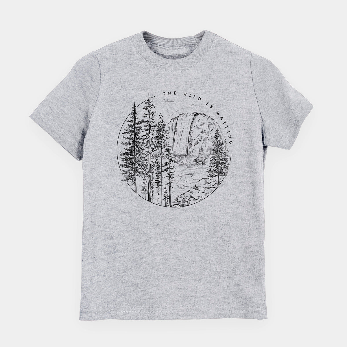 Heather grey youth t-shirt laid flat, printed with a round black ink scene of a waterfall, pine trees and a river, with the words The Wild Is Waiting.
