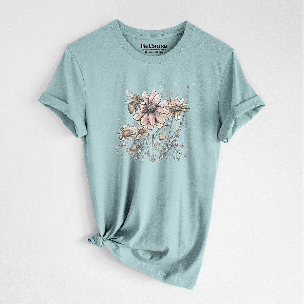 Dusty blue lightweight cotton t-shirt laid flat with the sleeves rolled, printed with a soft full-color illustration of a bee flying over pink and purple wildflowers.