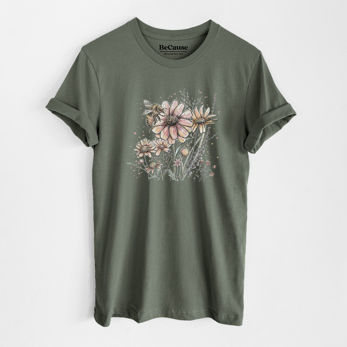 Military green lightweight cotton t-shirt laid flat, printed with a soft full-color illustration of a bee flying over pink and purple wildflowers.