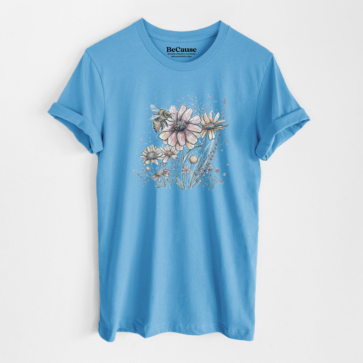 Ocean blue lightweight cotton t-shirt laid flat, printed with a soft full-color illustration of a bee flying over pink and purple wildflowers.