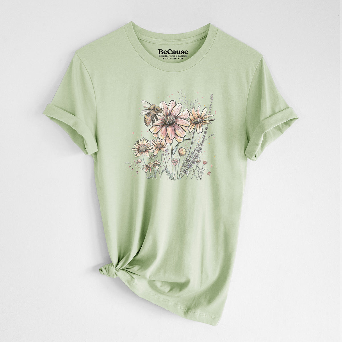Spring green lightweight cotton t-shirt laid flat with the sleeves rolled, printed with a soft full-color illustration of a bee flying over pink and purple wildflowers.