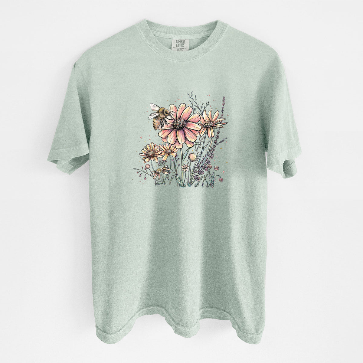 Bay green Comfort Colors t-shirt laid flat, printed with a soft full-color illustration of a bee flying over pink and purple wildflowers.