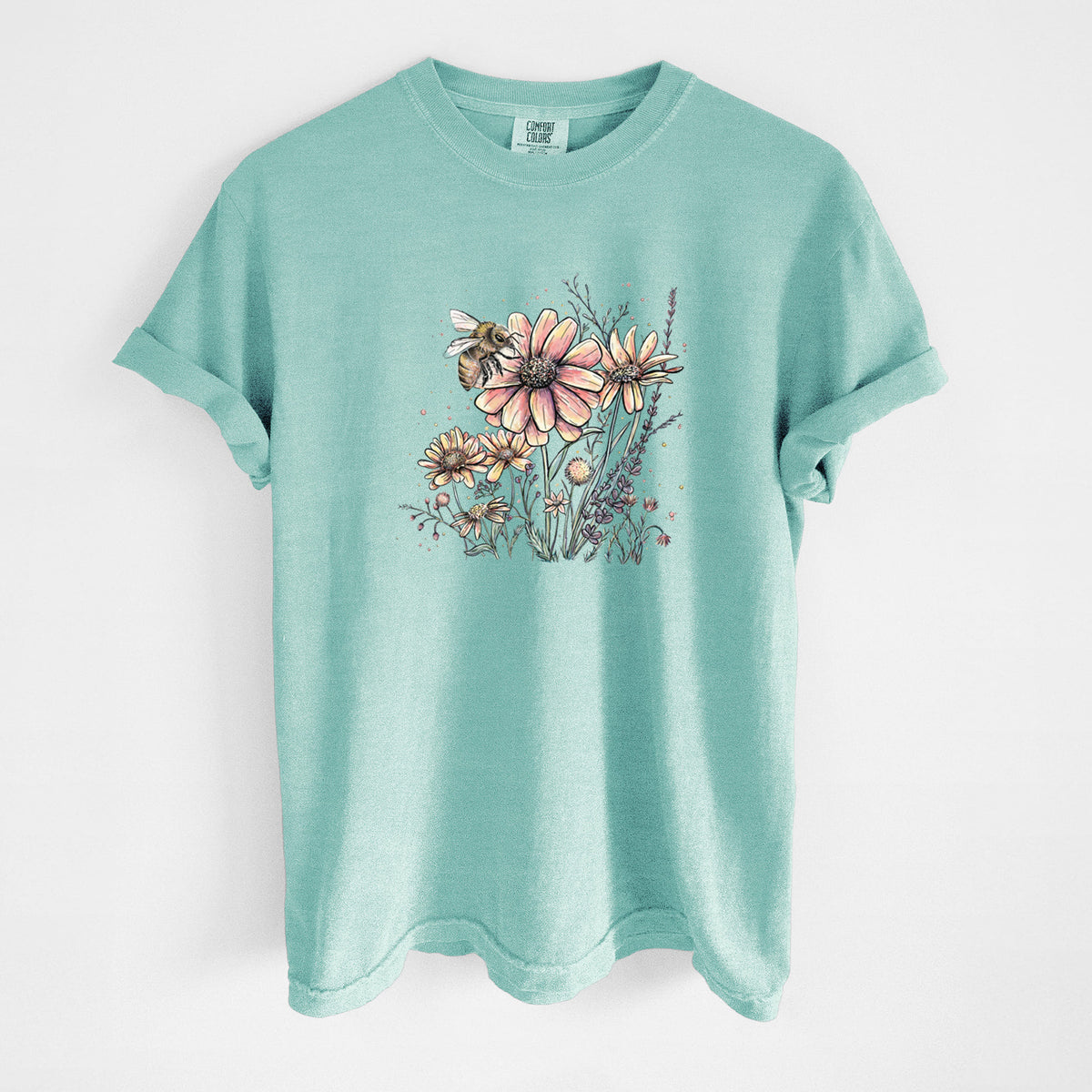 Chalky mint Comfort Colors t-shirt laid flat, printed with a soft full-color illustration of a bee flying over pink and purple wildflowers.