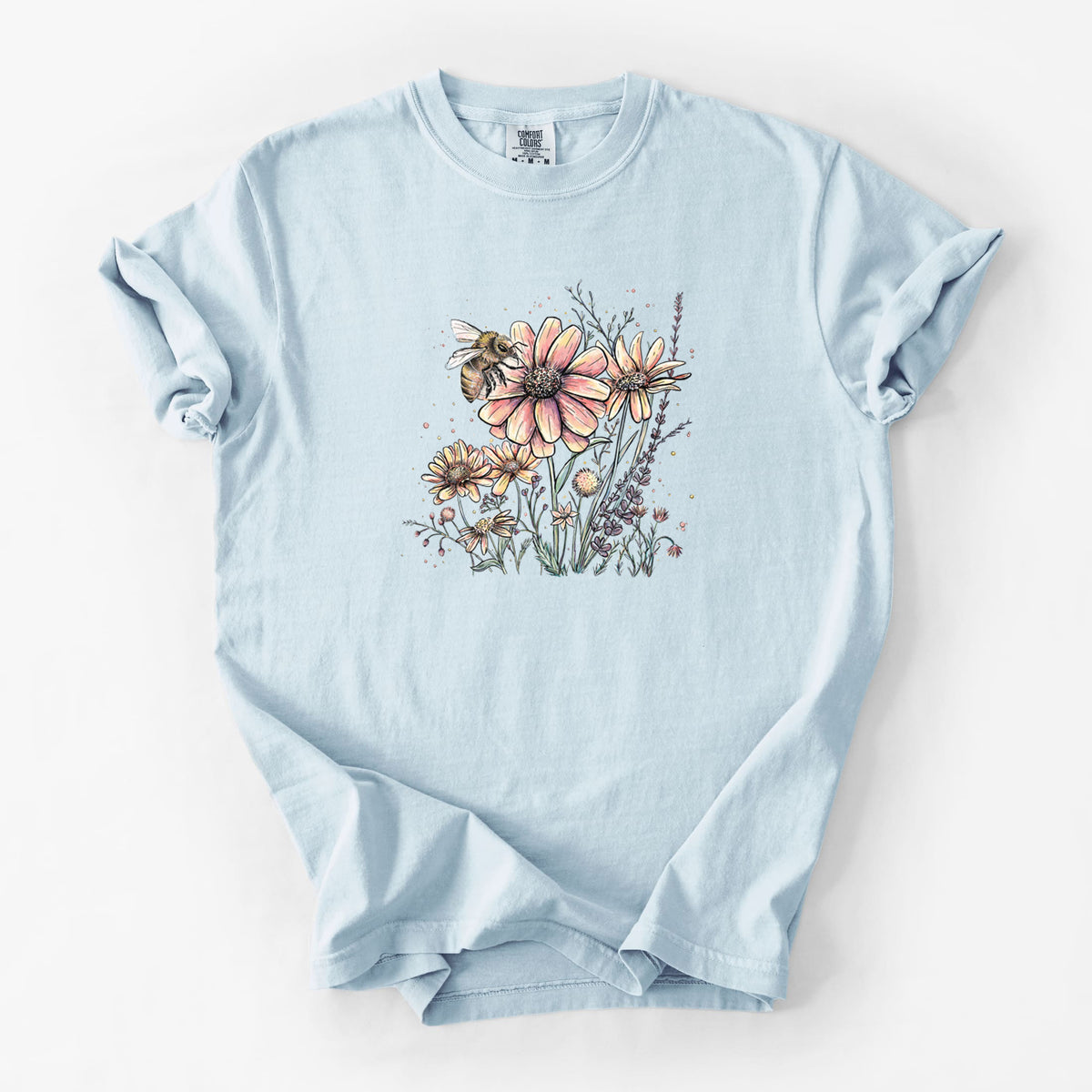 Chambray blue Comfort Colors t-shirt laid flat, printed with a soft full-color illustration of a bee flying over pink and purple wildflowers.