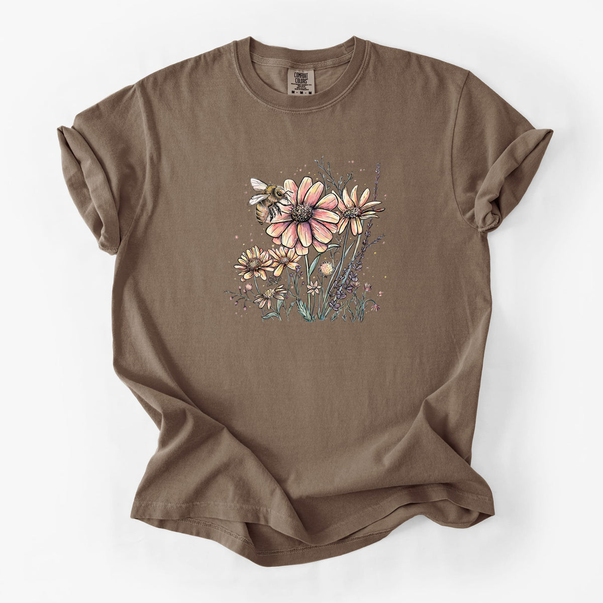 Espresso brown Comfort Colors t-shirt laid flat, printed with a soft full-color illustration of a bee flying over pink and purple wildflowers.