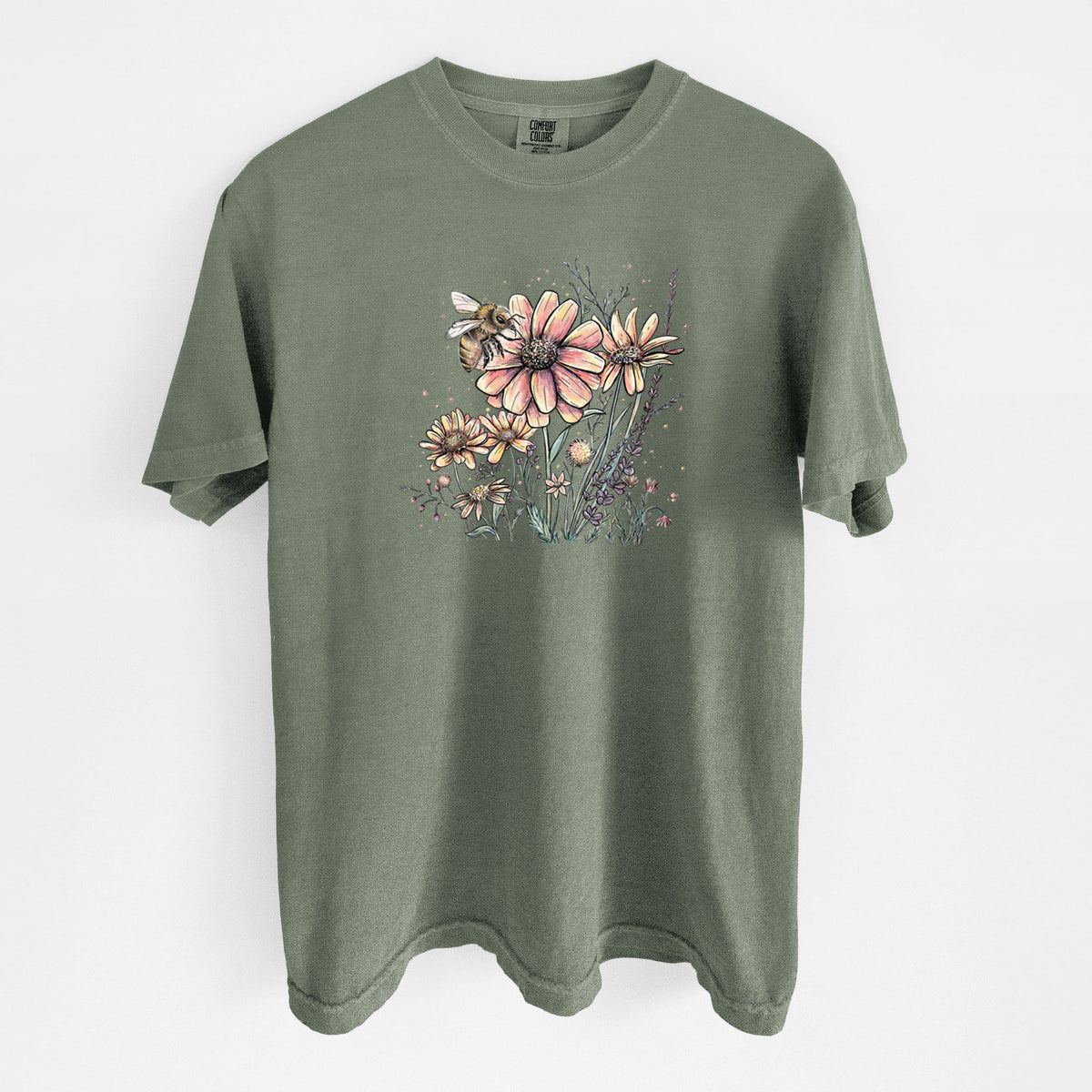 Moss green Comfort Colors t-shirt laid flat, printed with a soft full-color illustration of a bee flying over pink and purple wildflowers.