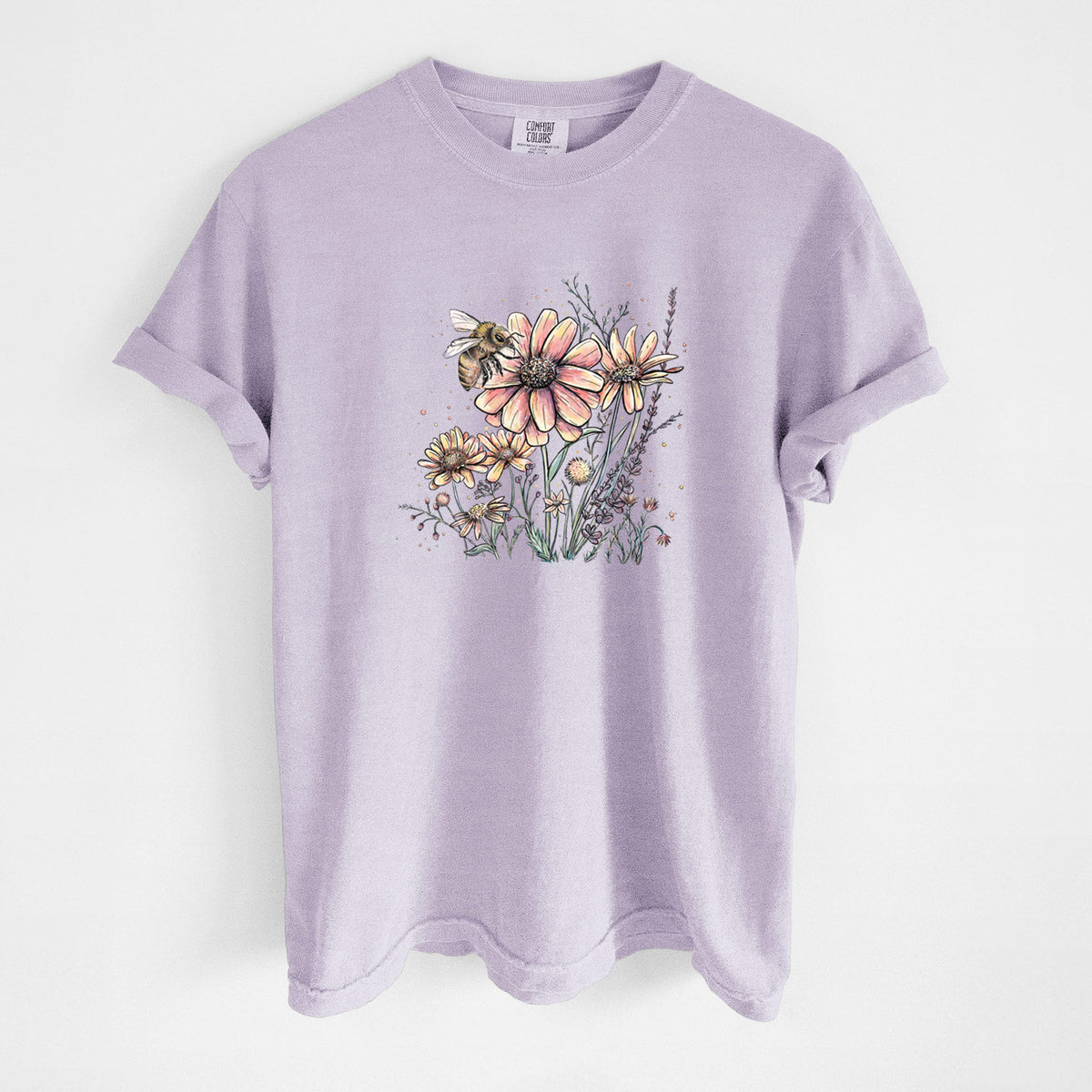 Orchid purple Comfort Colors t-shirt laid flat, printed with a soft full-color illustration of a bee flying over pink and purple wildflowers.