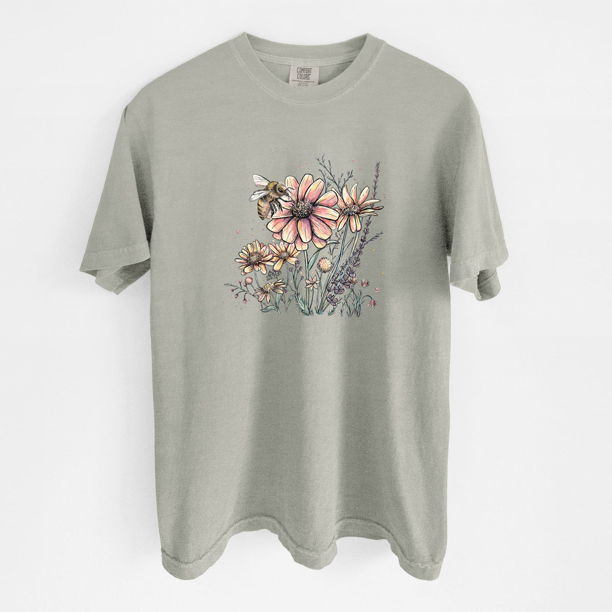 Sandstone beige Comfort Colors t-shirt laid flat, printed with a soft full-color illustration of a bee flying over pink and purple wildflowers.