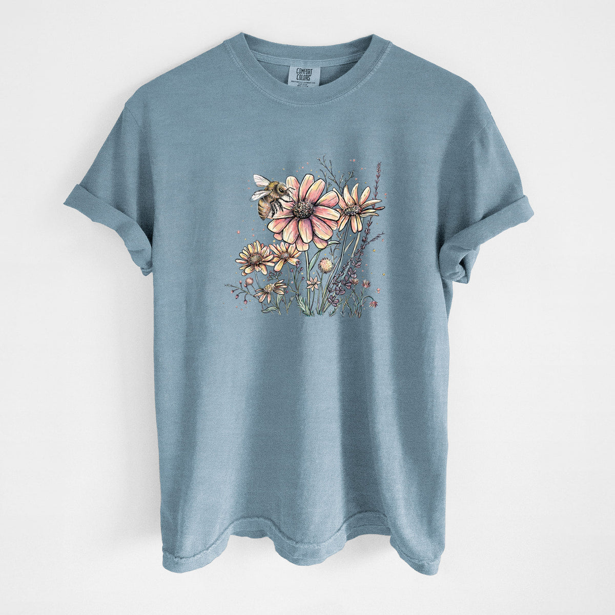 Steel blue Comfort Colors t-shirt laid flat, printed with a soft full-color illustration of a bee flying over pink and purple wildflowers.